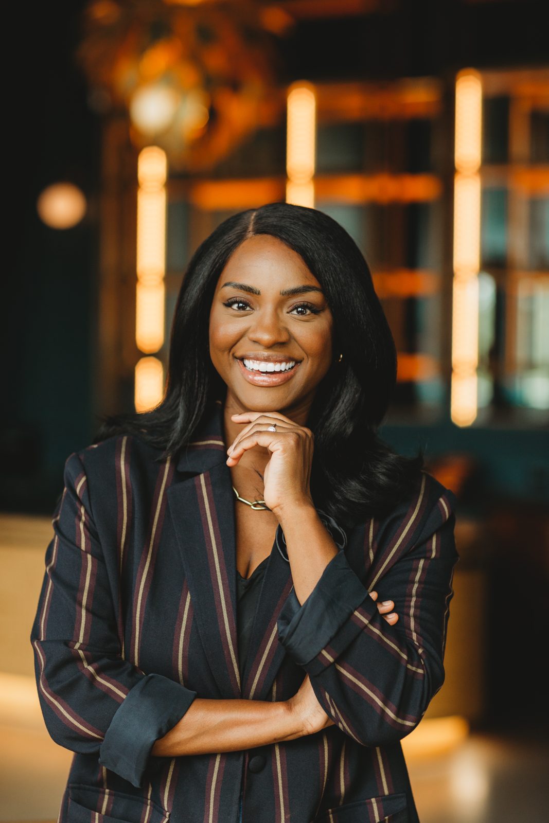 Danielle smiling in a dark striped blazer in a warmly lit lounge